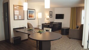 A hotel room with a dining area, a flat-screen TV, a sofa, and a trash bin. - Candlewood Suites Fort Collins by IHG (Fort Collins)