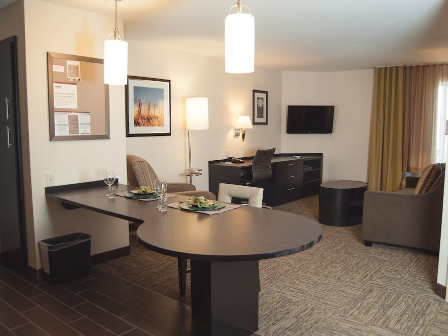 A hotel room with a dining area, a flat-screen TV, a sofa, and a trash bin.