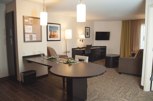 Een hotelkamer met een eethoek, een flatscreen televisie, een bank en een prullenbak.