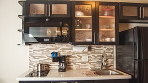 A modern kitchen with black cabinets, a stainless steel refrigerator, a coffee maker, and a microwave. - Candlewood Suites Fort Collins by IHG (Fort Collins)
