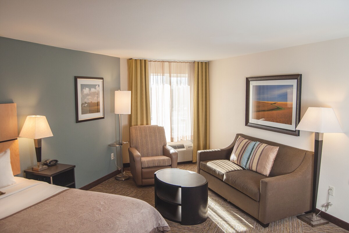 A hotel room with a bed, two armchairs, a sofa, a round coffee table, and two lamps.