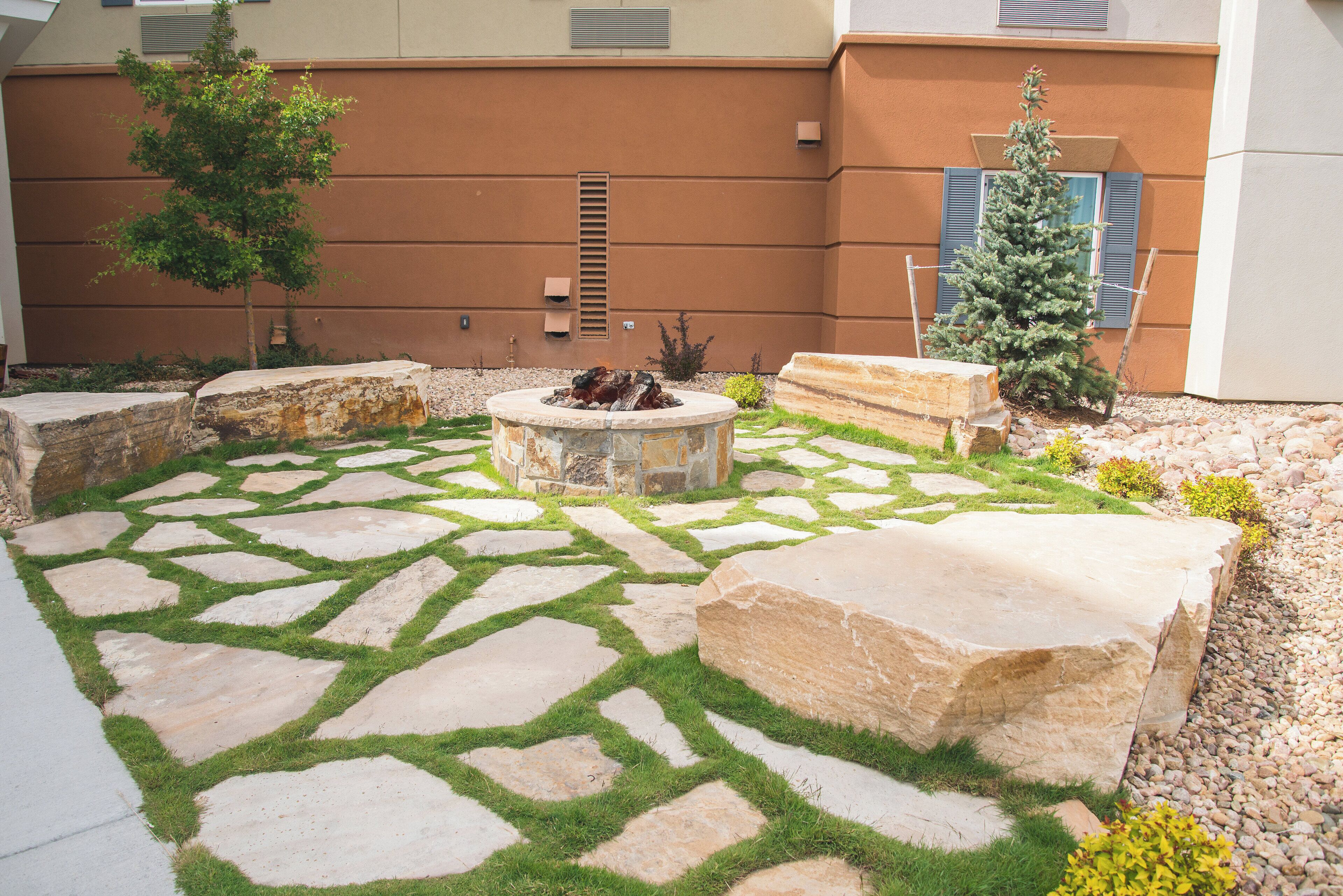 A courtyard with a stone fire pit surrounded by a patterned stone pathway and large rocks.