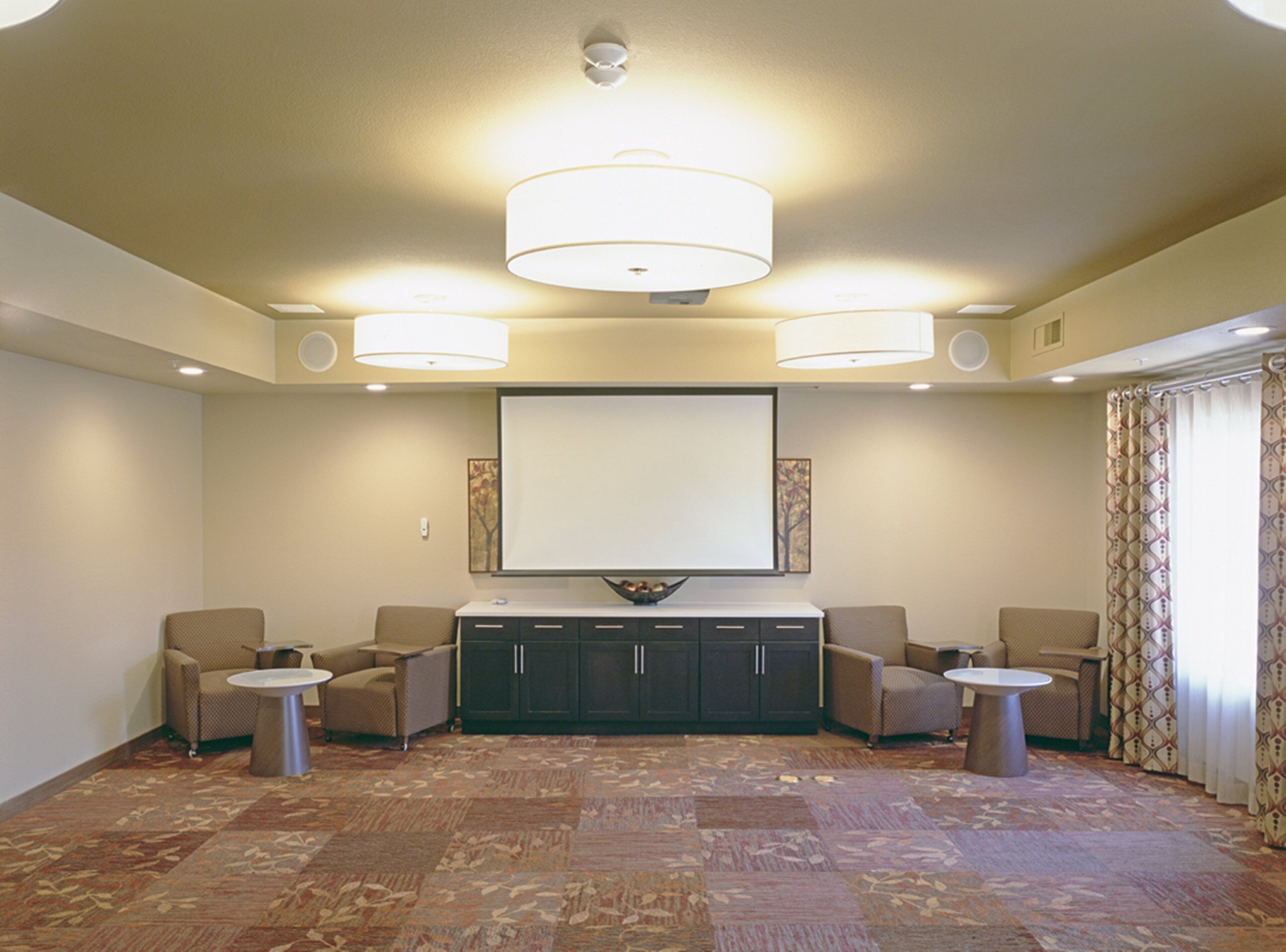 A spacious room with a large flat-screen TV mounted on the wall, a comfortable seating area with sofas and armchairs, and a patterned carpet.