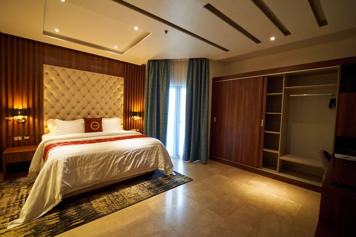 A modern hotel room with a large bed, built-in wardrobe, and a cozy seating area.
