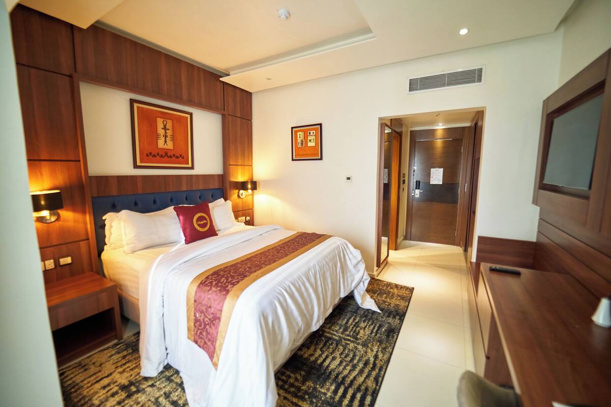 A hotel room with a large bed, wooden headboard, bedside lamps, a desk, and a television.