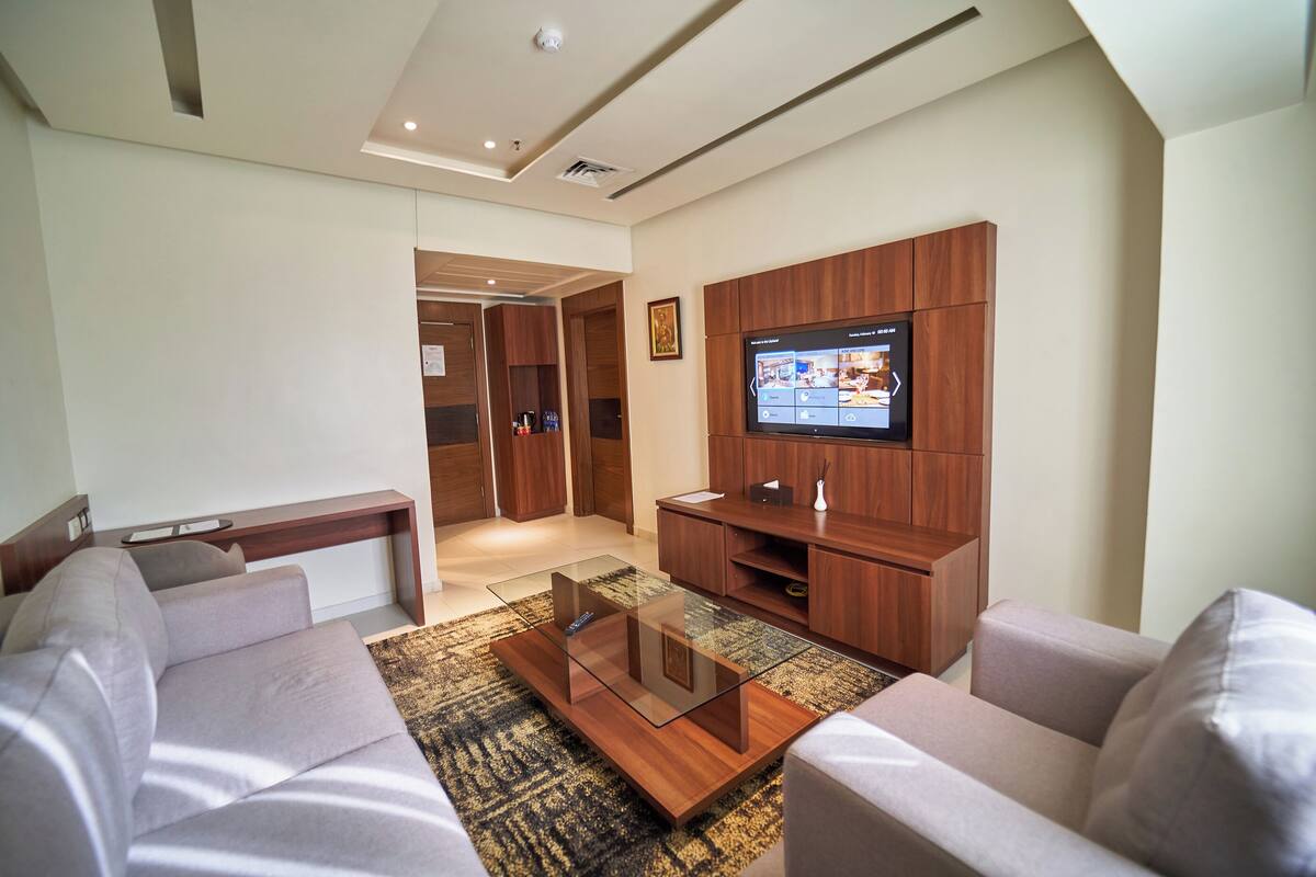 A modern living room with a glass coffee table, a flat-screen TV, wooden cabinets, and a sofa.