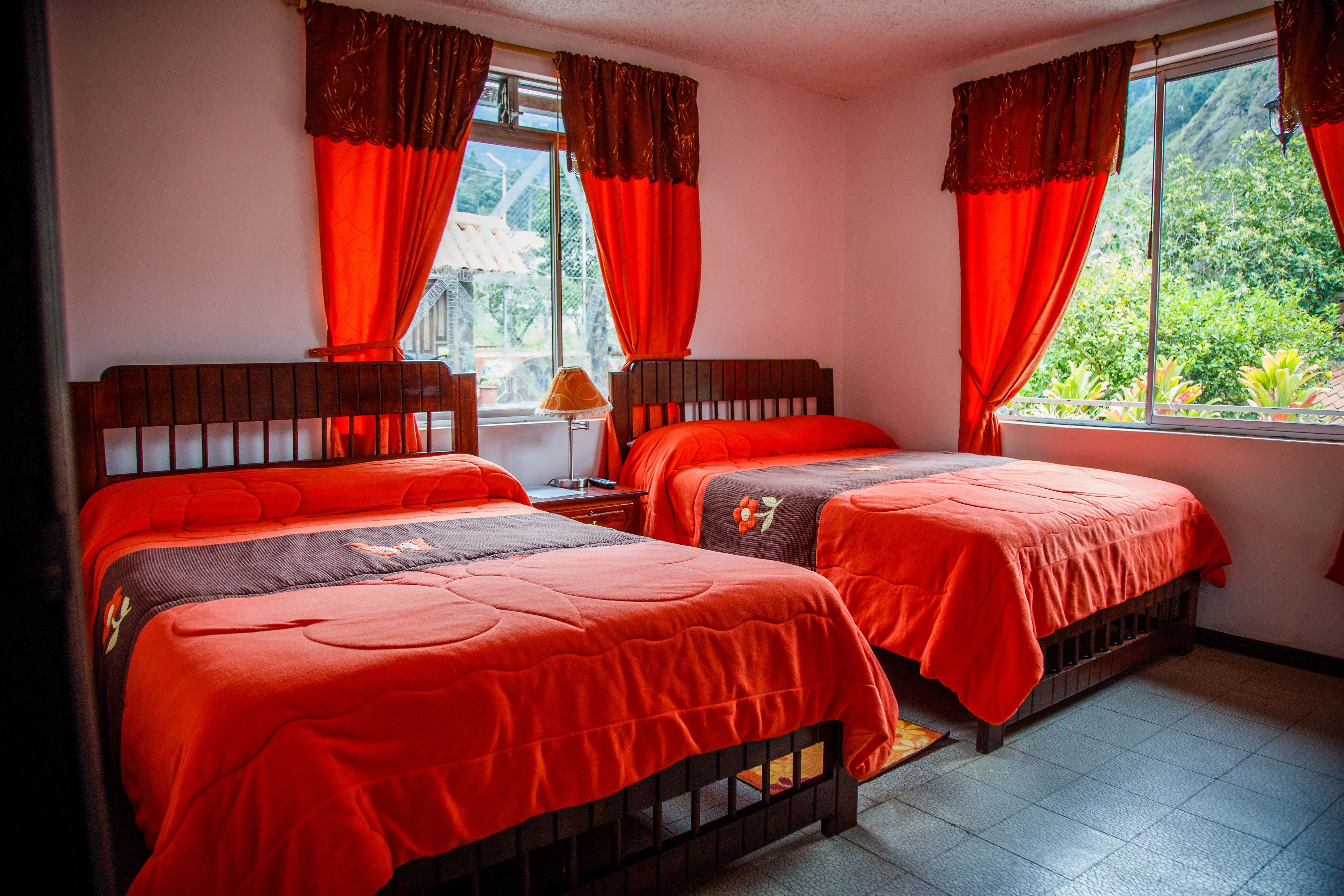 A room with two beds, red curtains, and a window with a view of greenery.