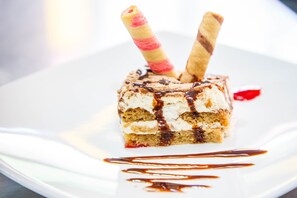 A dessert with chocolate drizzle and wafer sticks on a white plate. - Hosteria Jardines de Chamana (Ulba)