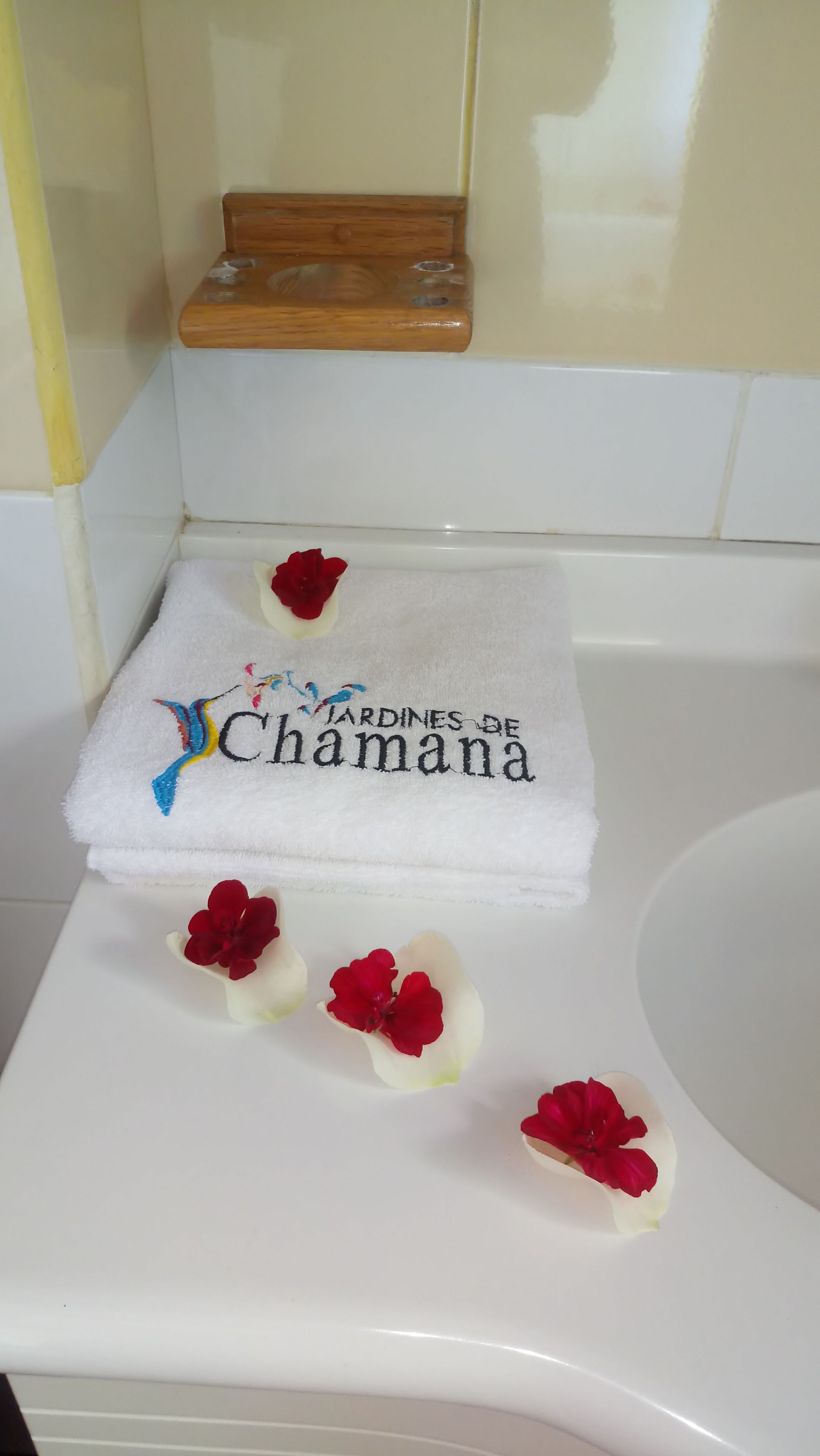 Un baño blanco con una bañera blanca, un estante de madera y una toalla con diseño floral y texto.