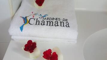 Un baño blanco con una bañera blanca, un estante de madera y una toalla con diseño floral y texto.