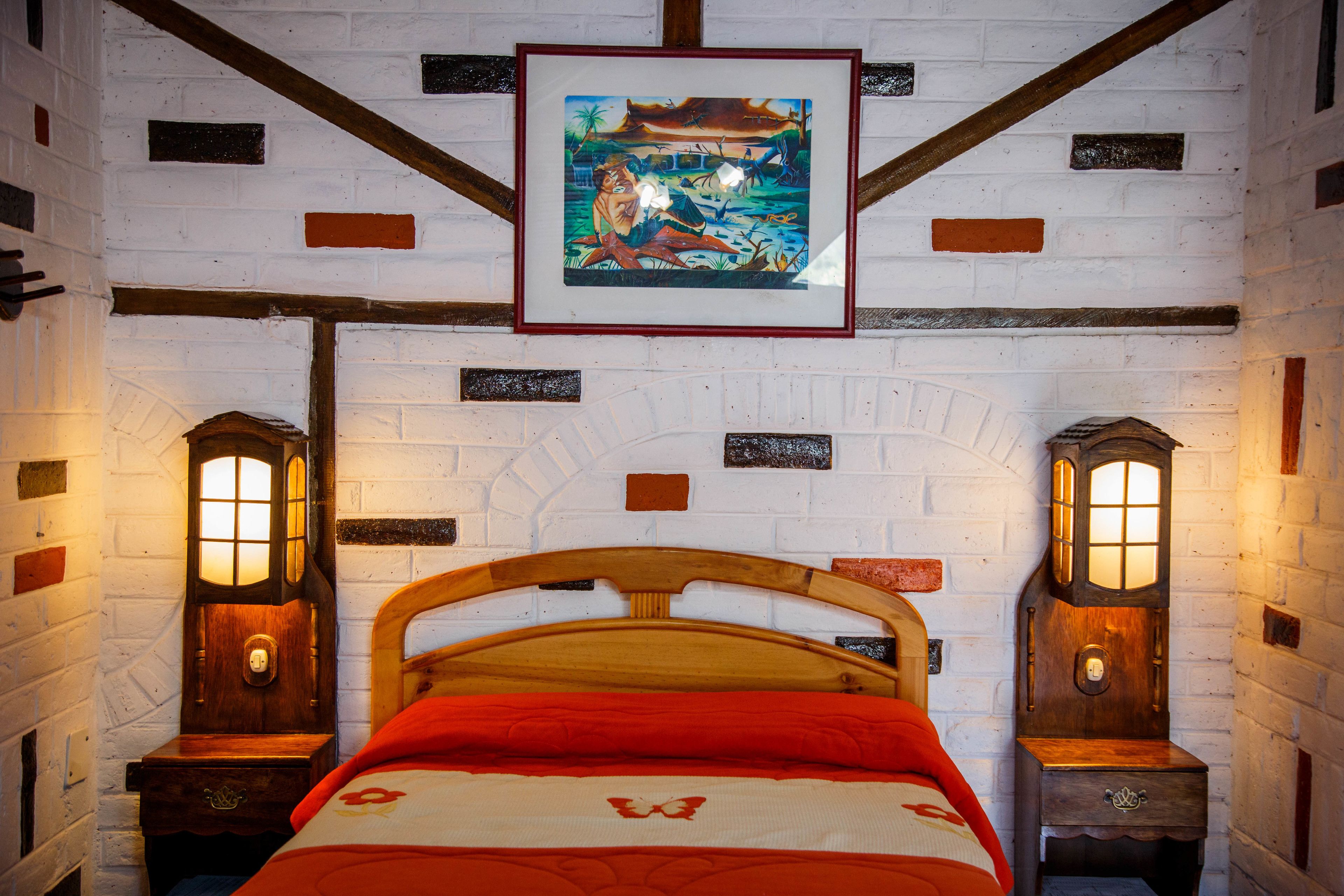Una habitación con una cama de madera, dos mesitas de noche con lámparas de pared, y un cuadro enmarcado sobre la cama.