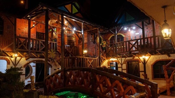 A rustic wooden building with a balcony and a small pond. - Hosteria Jardines de Chamana (Ulba)