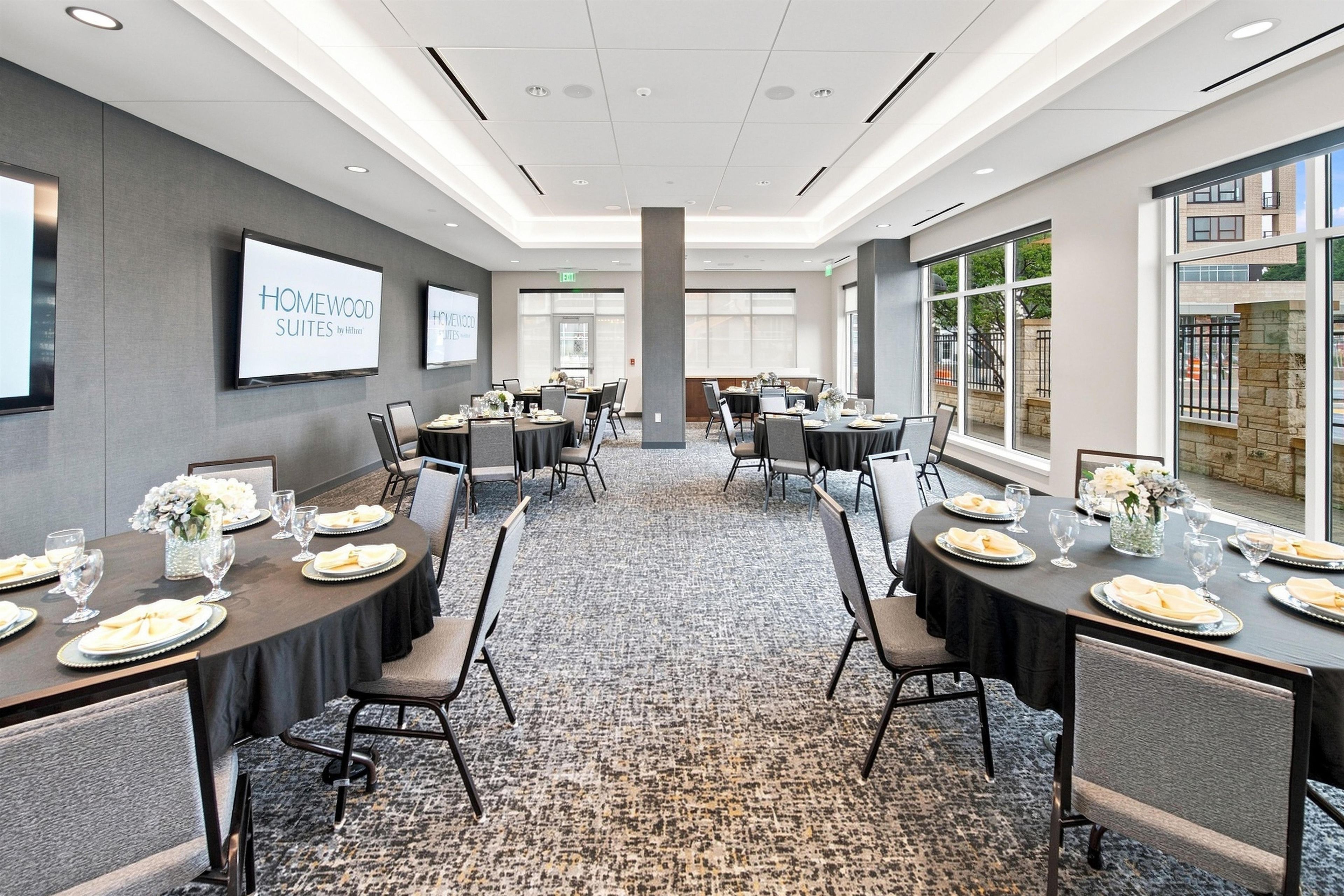 A conference room with tables set for a meeting, a projector screen, and a view of the outside.