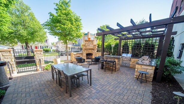 An outdoor patio with a brick floor, stone fireplace, and wooden pergola. - Homewood Suites by Hilton Rochester Mayo Clinic Area / Saint Marys (Rochester)
