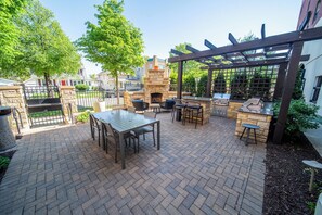 Une terrasse extérieure avec un sol en briques, une cheminée en pierre et une pergola en bois.