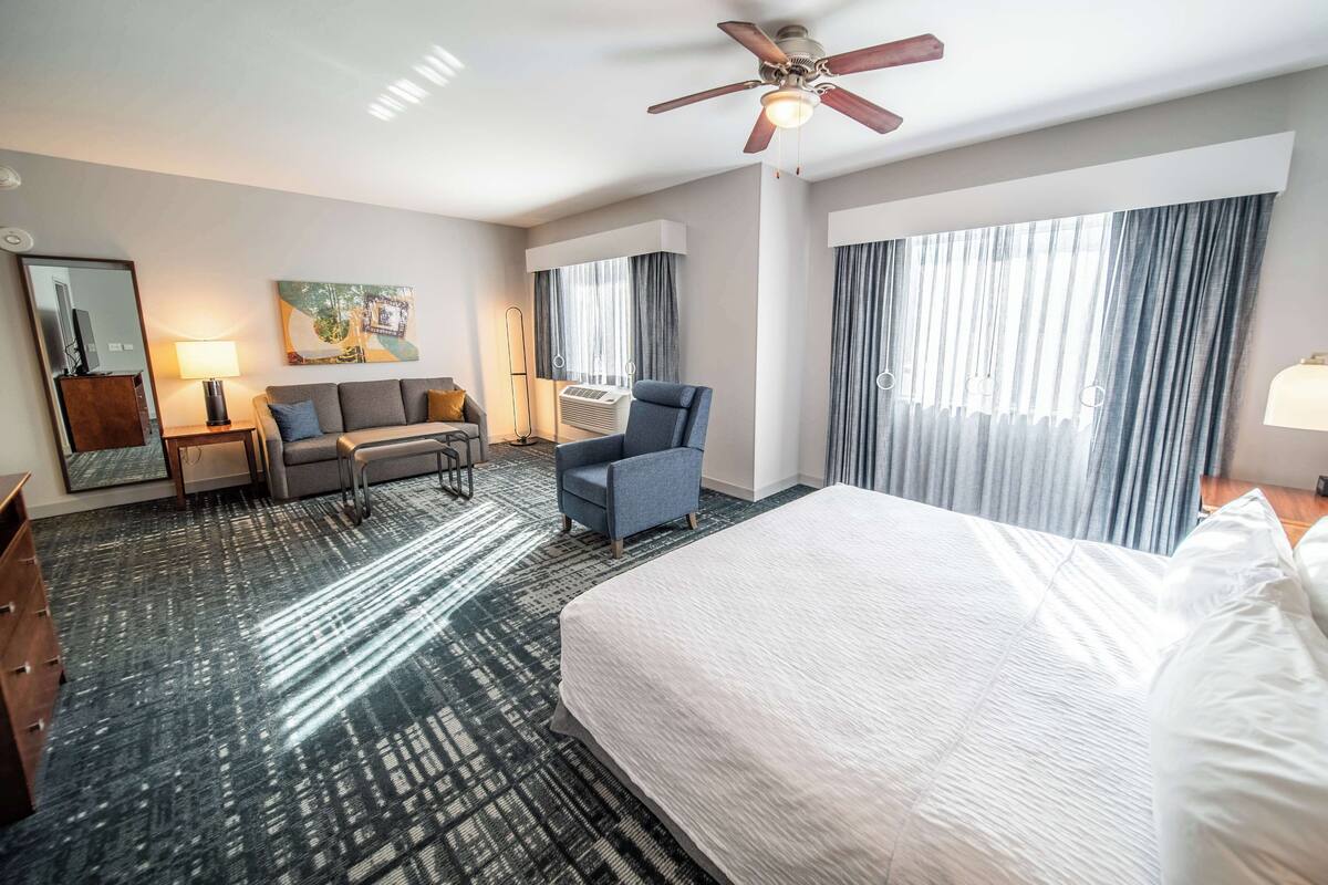Een hotelkamer met een groot bed, een bank, een stoel, een bureau en een plafondventilator.