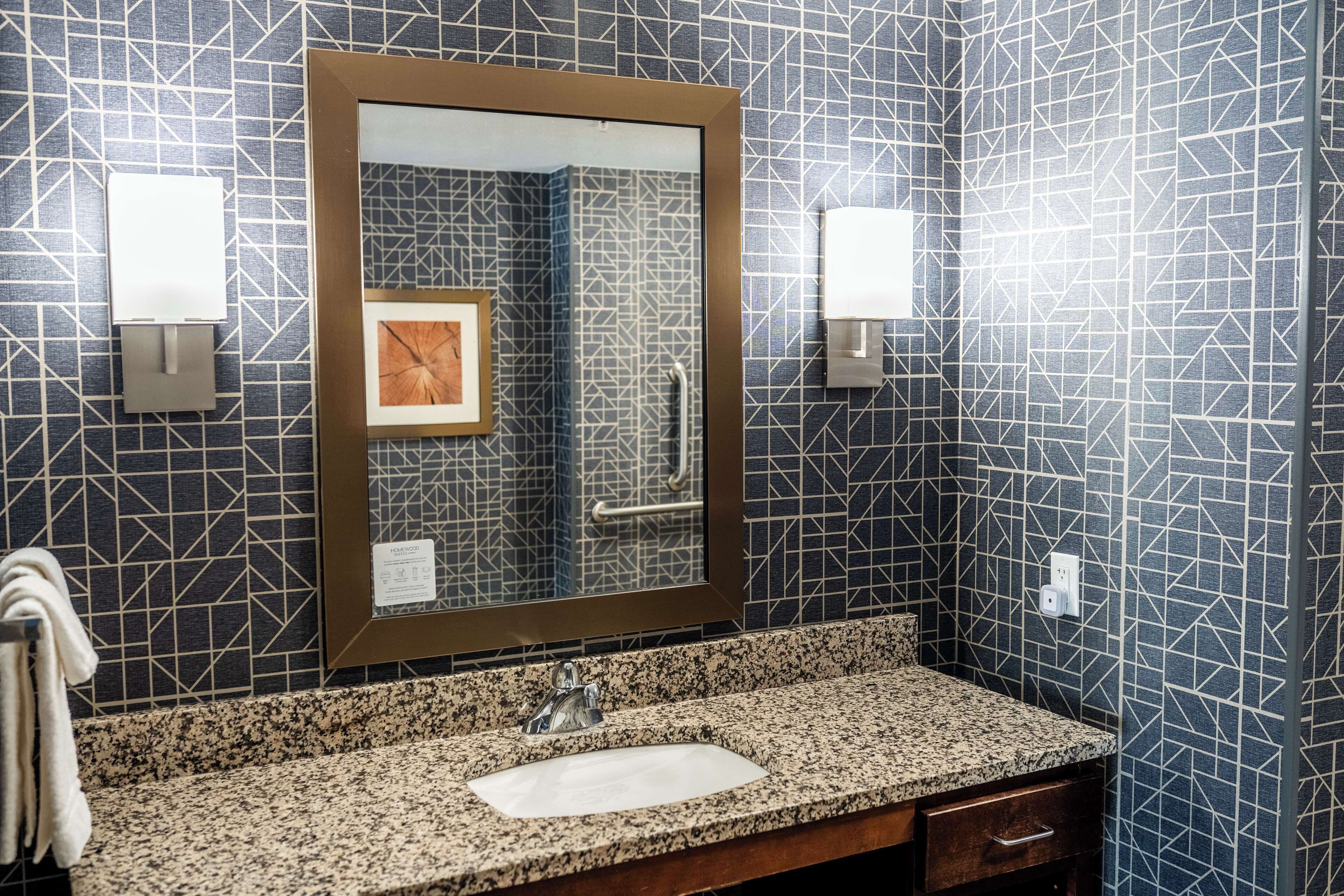 A bathroom with a granite countertop, a sink, a mirror, and a towel rack.
