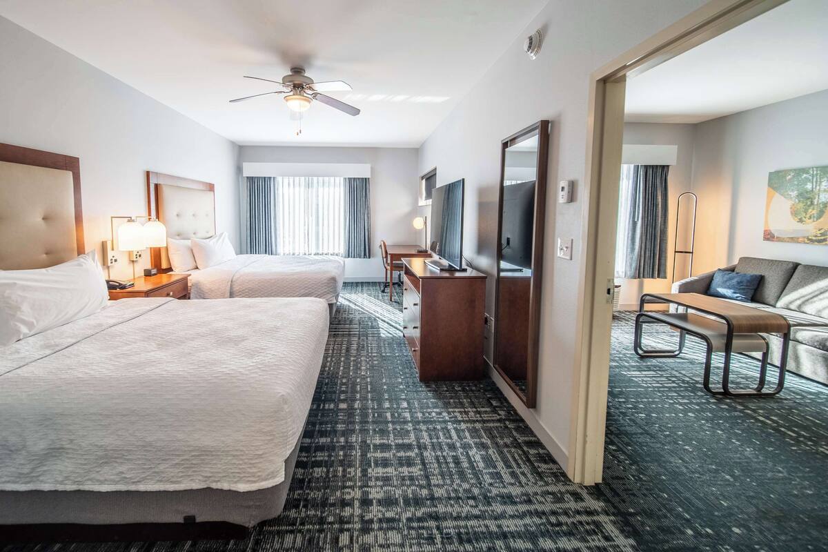 Een hotelkamer met twee bedden, een bureau, een stoel, een televisie en een plafondventilator.