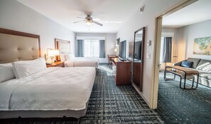 Une chambre d’hôtel avec deux lits, un bureau, une chaise, une télévision et un ventilateur de plafond.