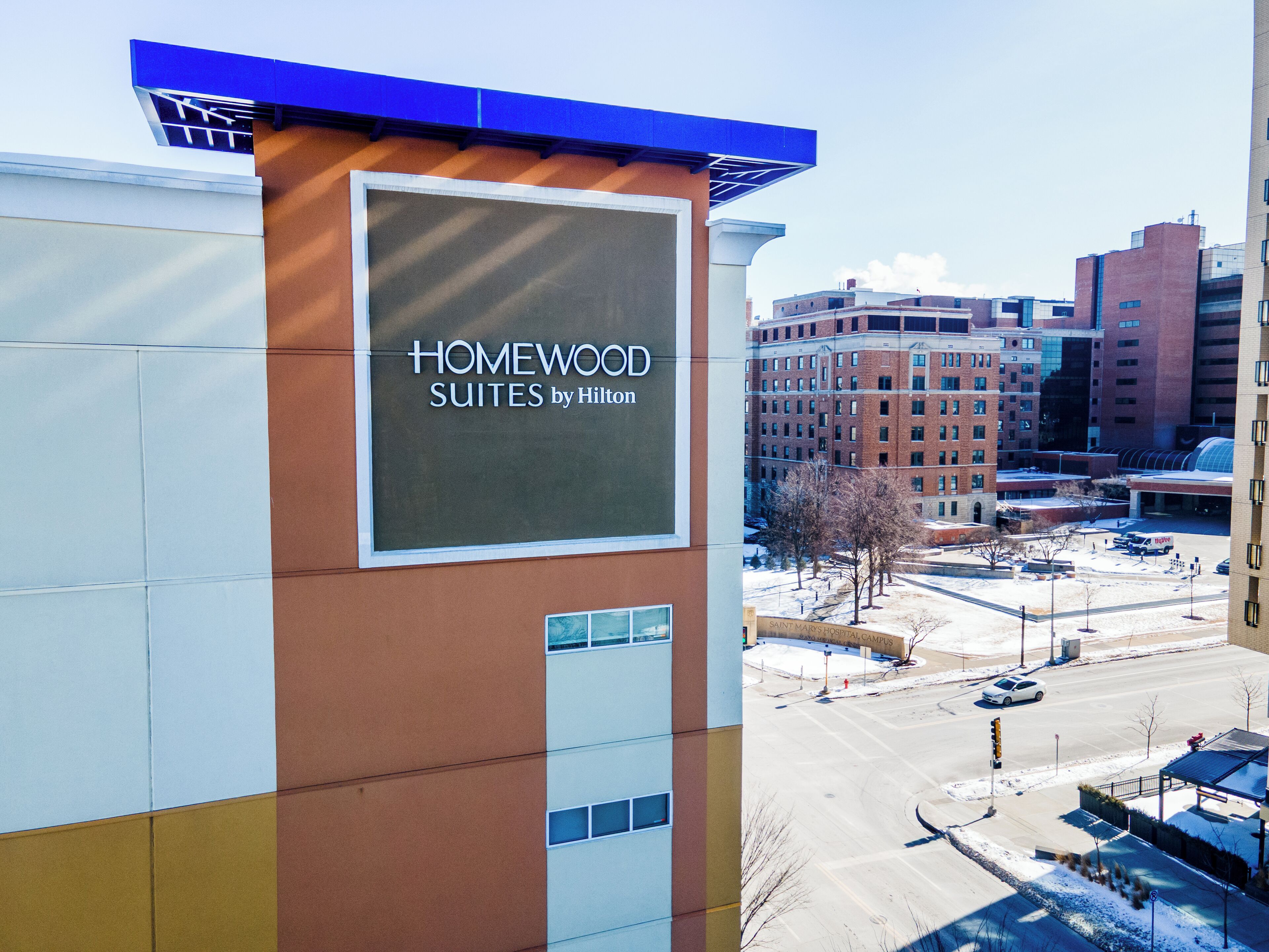 A hotel sign with 'HOMEWOOD SUITES by Hilton' and a view of the surrounding urban area.