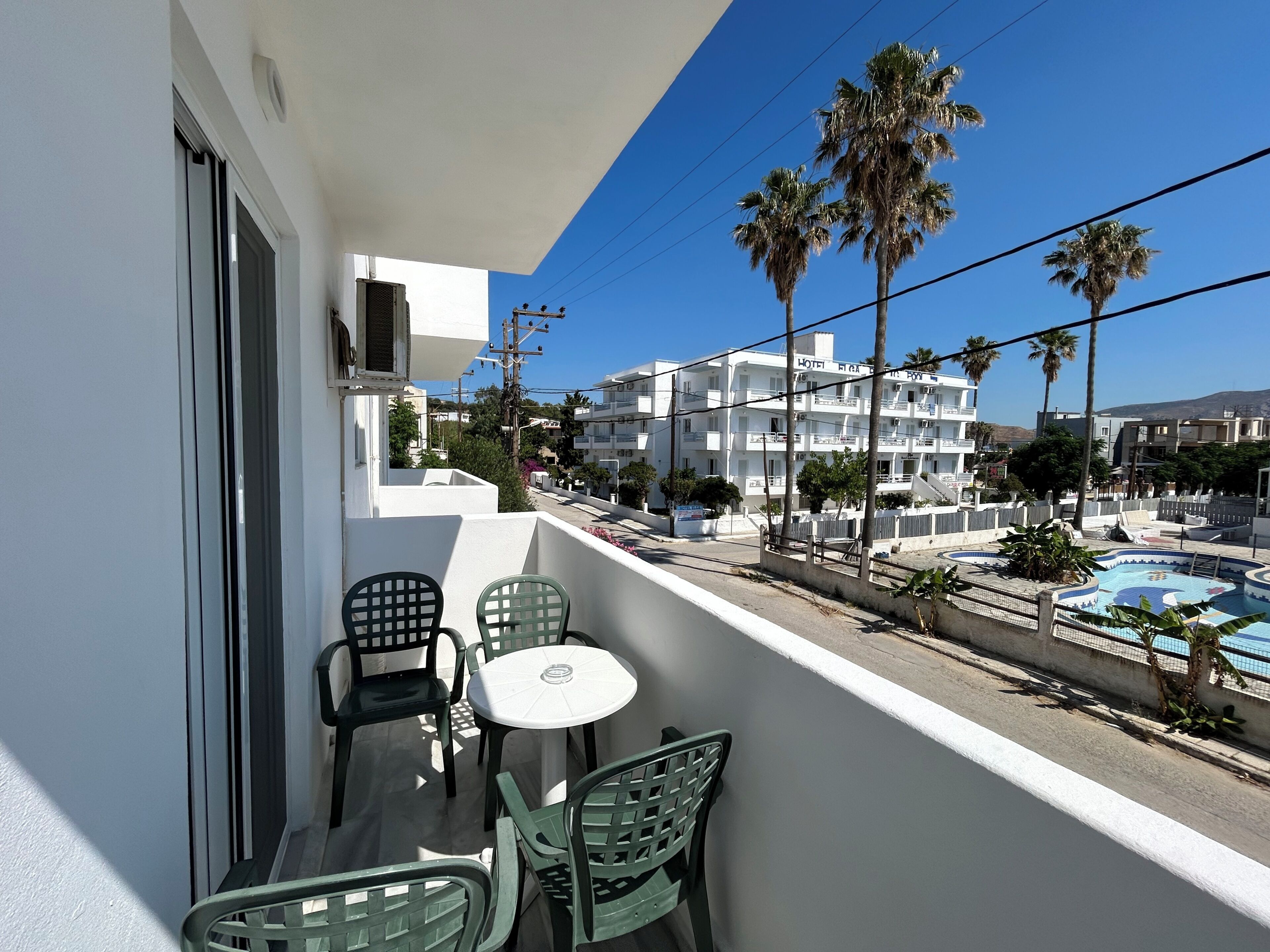 Un balcon avec des chaises et une table, donnant sur une piscine et un bâtiment d’hôtel.