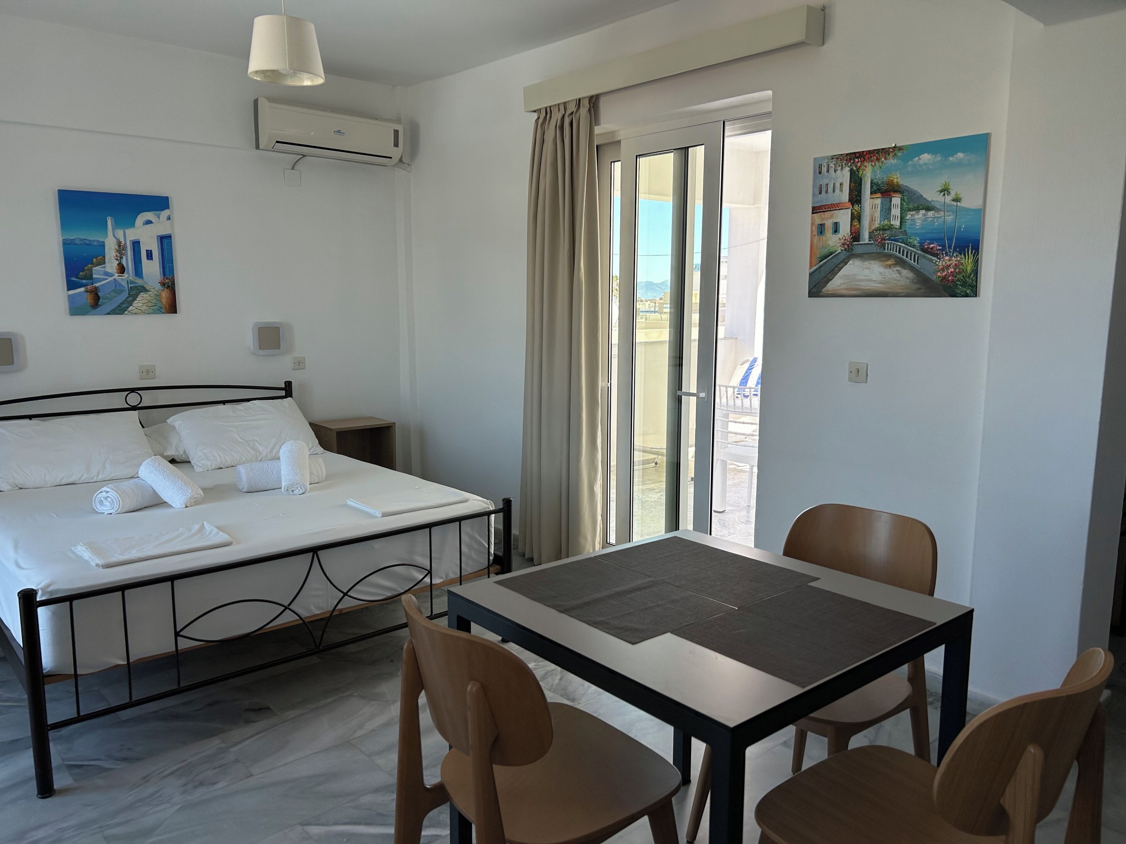 A hotel room with a bed, a table with chairs, a painting, and a view through the window.