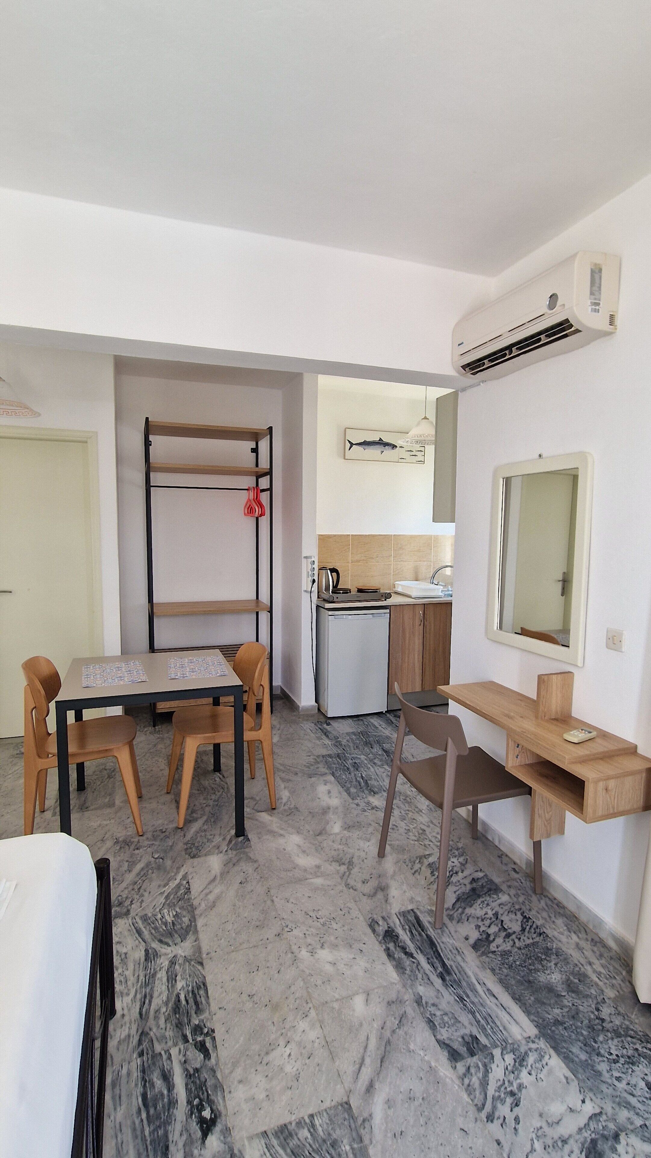 Habitación compacta con una mesa de comedor, sillas, una pequeña kitchenette, un espejo y un escritorio integrado.