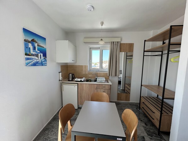 A compact kitchen with a sink, a small refrigerator, and a dining area with a table and chairs. - Kaloxenia Apartments (Kos)