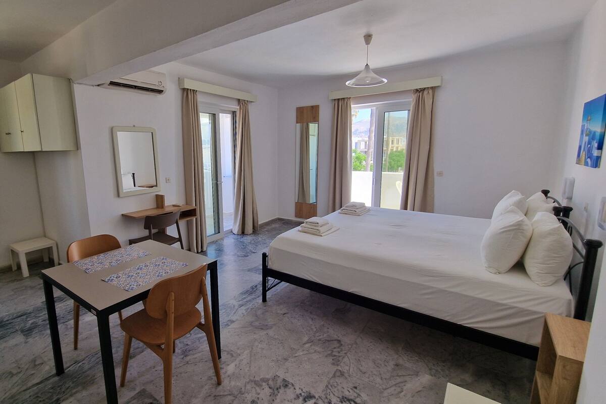 A hotel room with a bed, a desk, a chair, a small table, and a window with curtains.