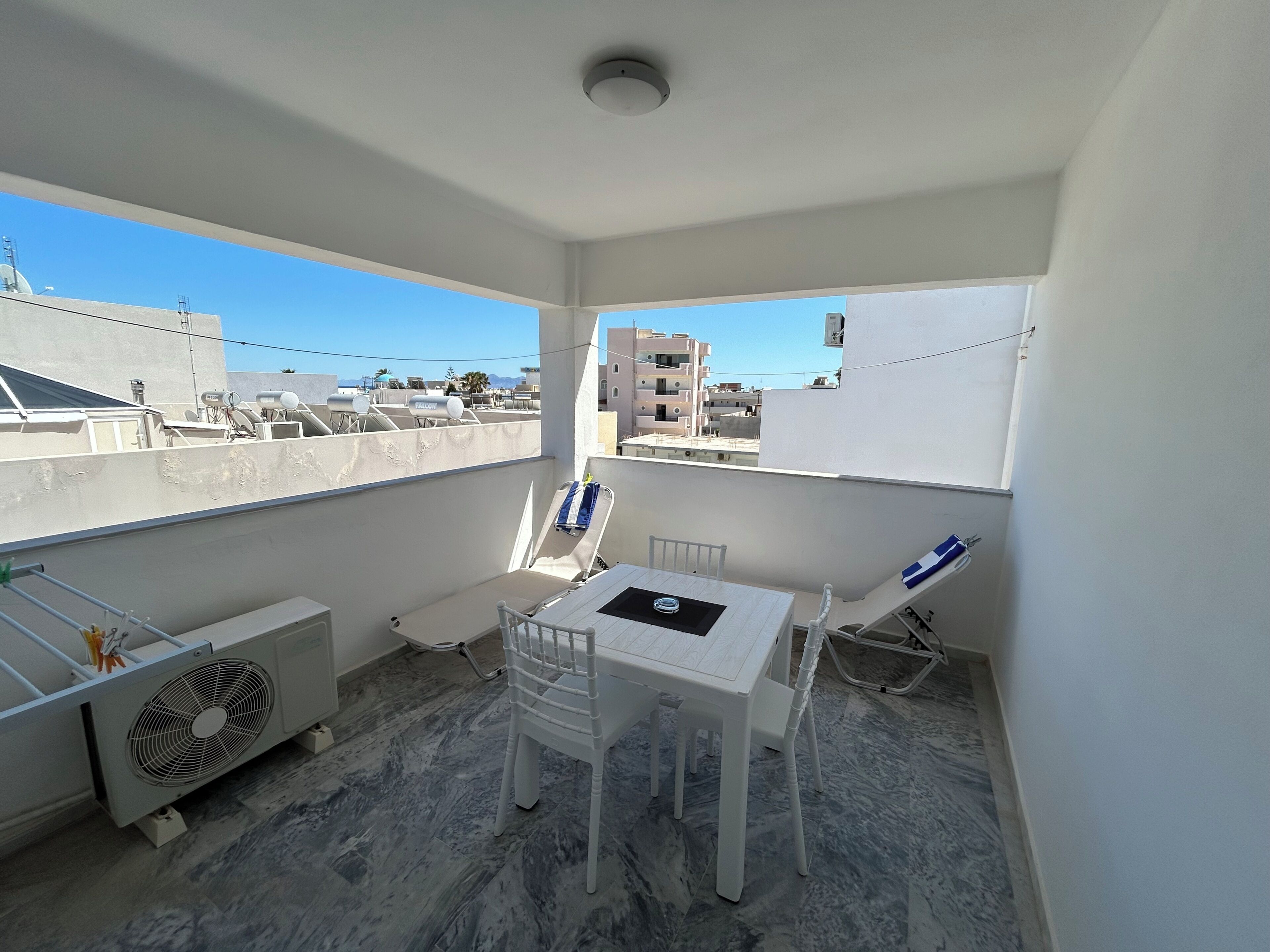 A small balcony with a table and chairs, an air conditioning unit, and a view of buildings.