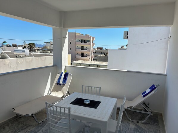 A balcony with a table and chairs, a view of buildings, and a water tank labeled 'FALCON'. - Kaloxenia Apartments (Kos)