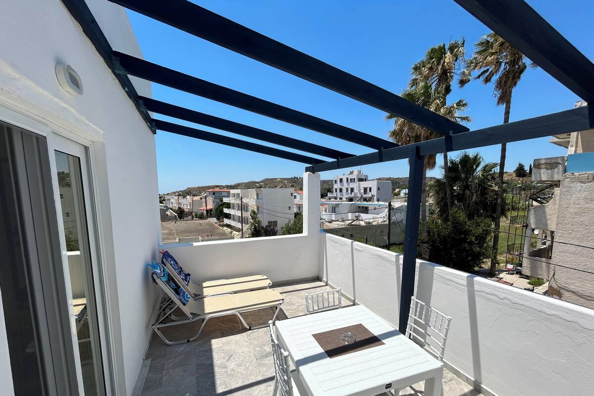 A balcony with a table and chairs, a view of buildings, and a palm tree.
