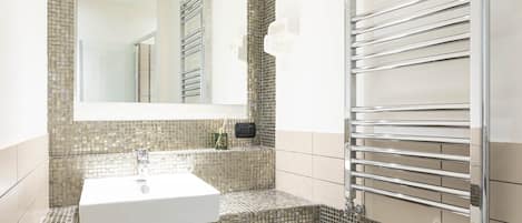 Un baño con un lavamanos blanco, un espejo grande y un toallero de cromo.