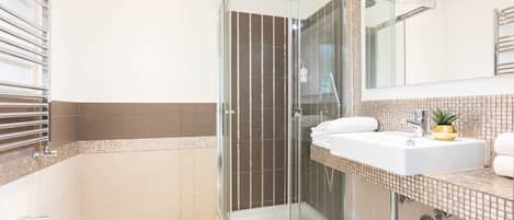 Un baño moderno con ducha de vidrio, lavabo blanco y espejo grande.