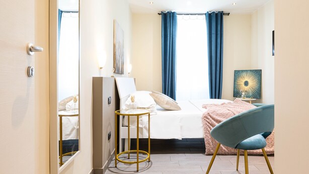 A hotel room with a bed, a chair, a small table, a mirror, and a painting on the wall. - Cesar Vatican Rooms (Rome)