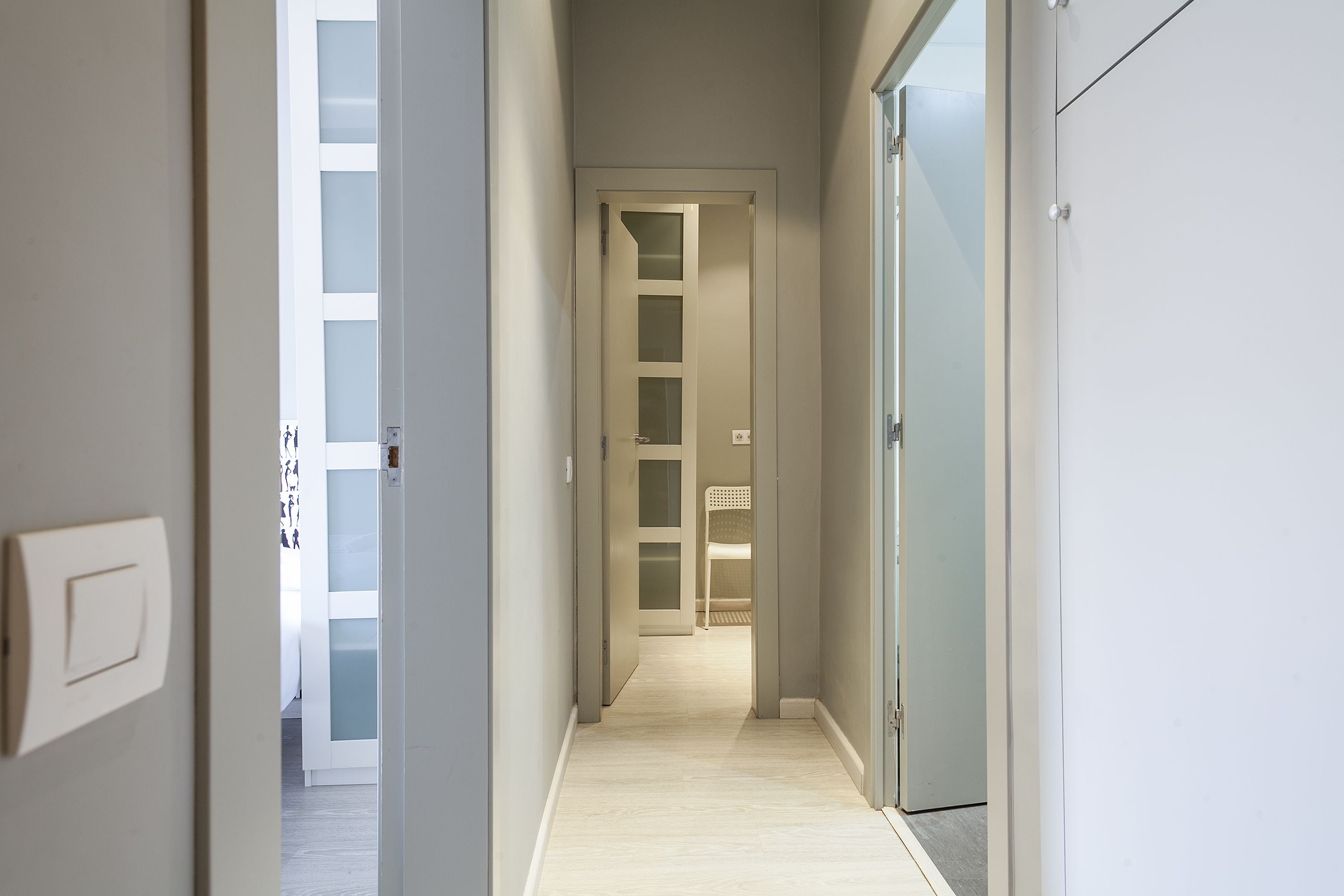 Un pasillo estrecho con piso de color claro que conduce a una habitación con puerta blanca y paneles de vidrio esmerilado.