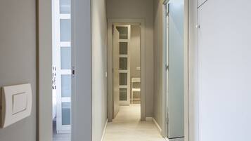 Un pasillo estrecho con piso de color claro que conduce a una habitación con puerta blanca y paneles de vidrio esmerilado.