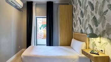 Una habitación de hotel con una cama, una mesita de noche con lámpara, una ventana con cortinas y una pared decorada con un diseño de hojas.