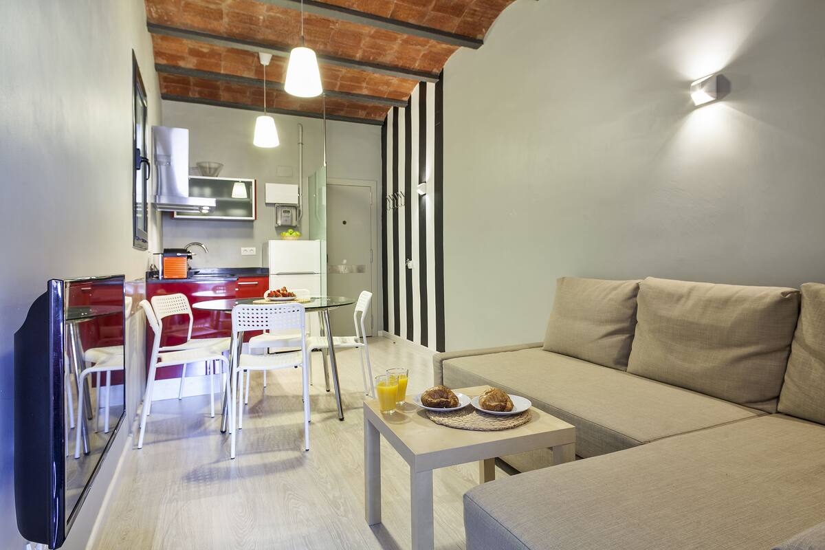 A modern living room with a sofa, a dining table with chairs, and a kitchen area in the background.