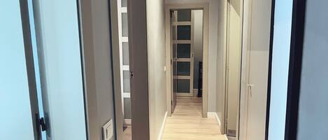 Un pasillo con suelo de madera, paredes grises y puertas que dan a otras habitaciones.