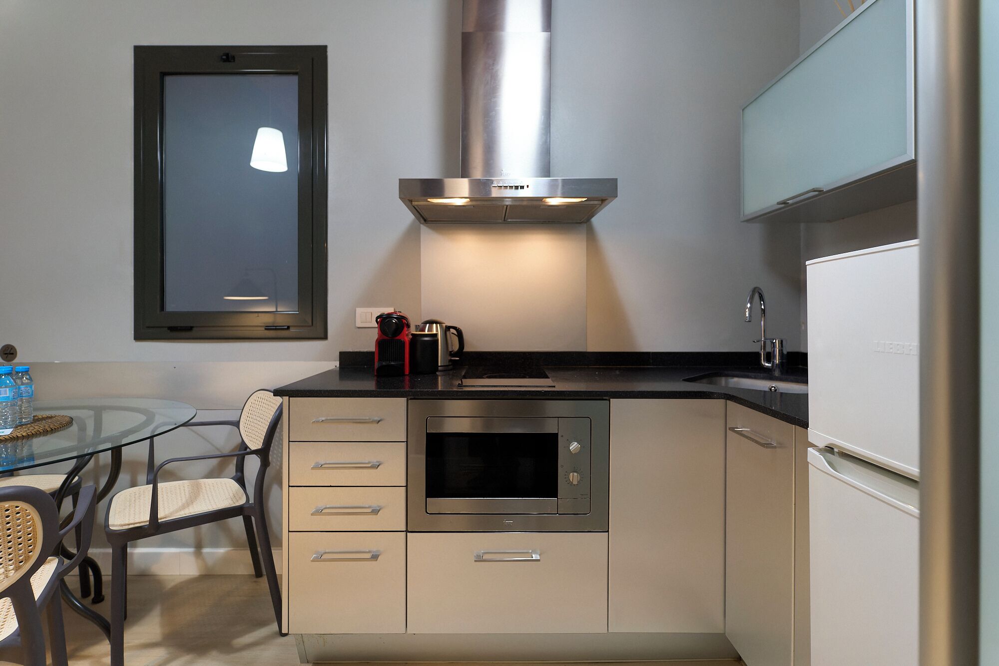 A compact kitchen with a built-in oven, a coffee maker, and a stainless steel range hood.