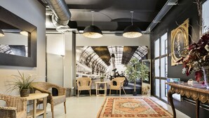 A modern interior with wicker furniture, a patterned rug, and a large window with a view of a building's interior.