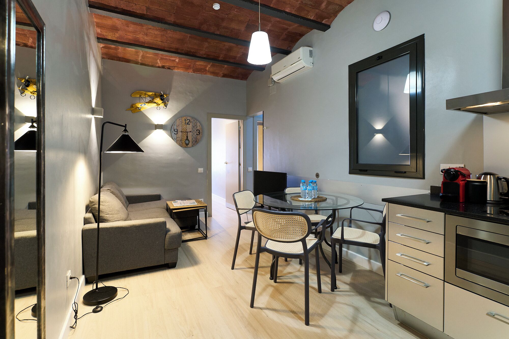 Un espace de vie moderne comprenant un canapé, une table à manger, des chaises, un coin cuisine et un grand miroir.