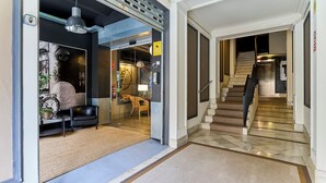 A modern hotel lobby with a glass door entrance, a staircase, and a seating area with a sofa and a small table.