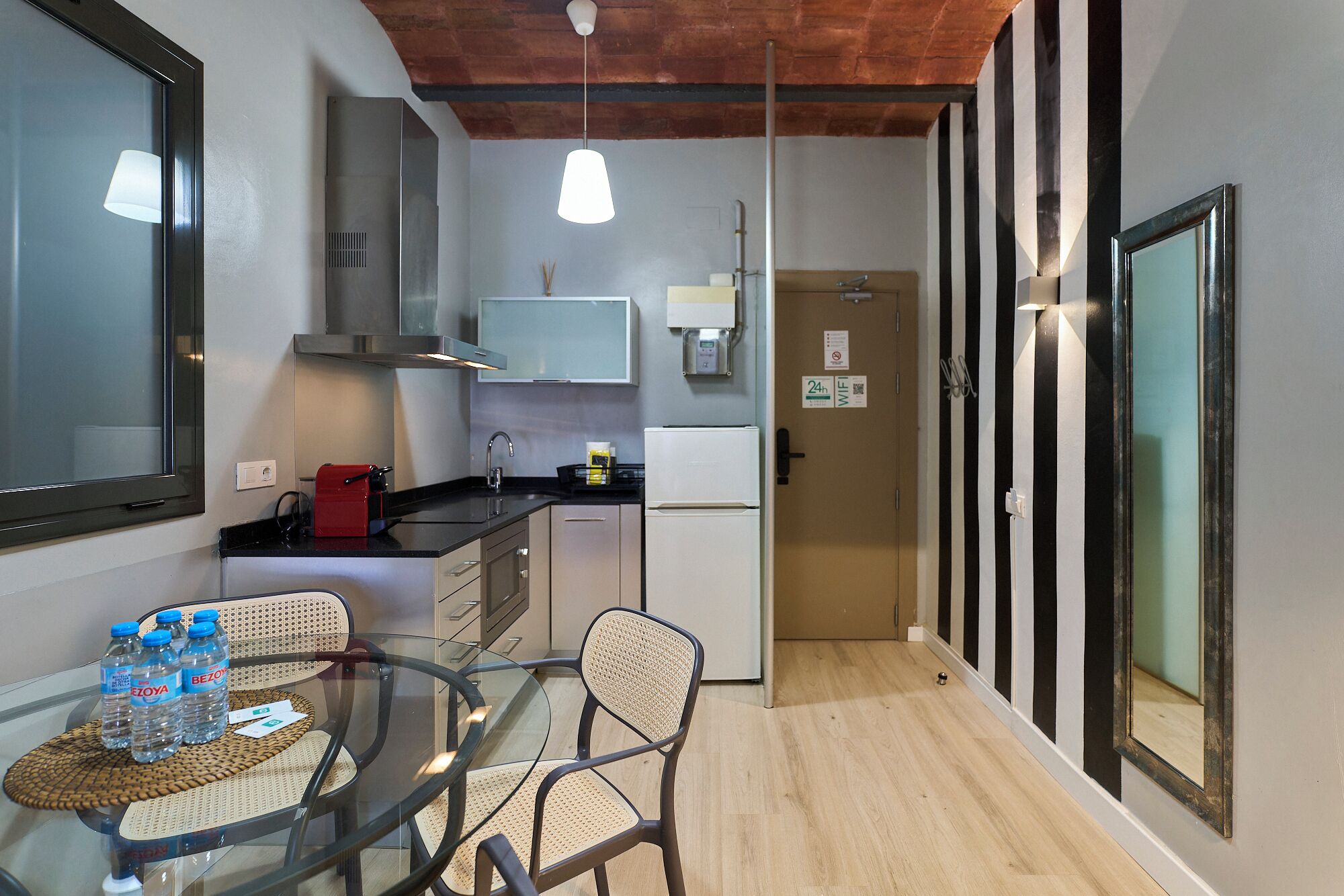 Une cuisine de taille réduite avec une table en verre, des chaises, un grille-pain rouge et un réfrigérateur.