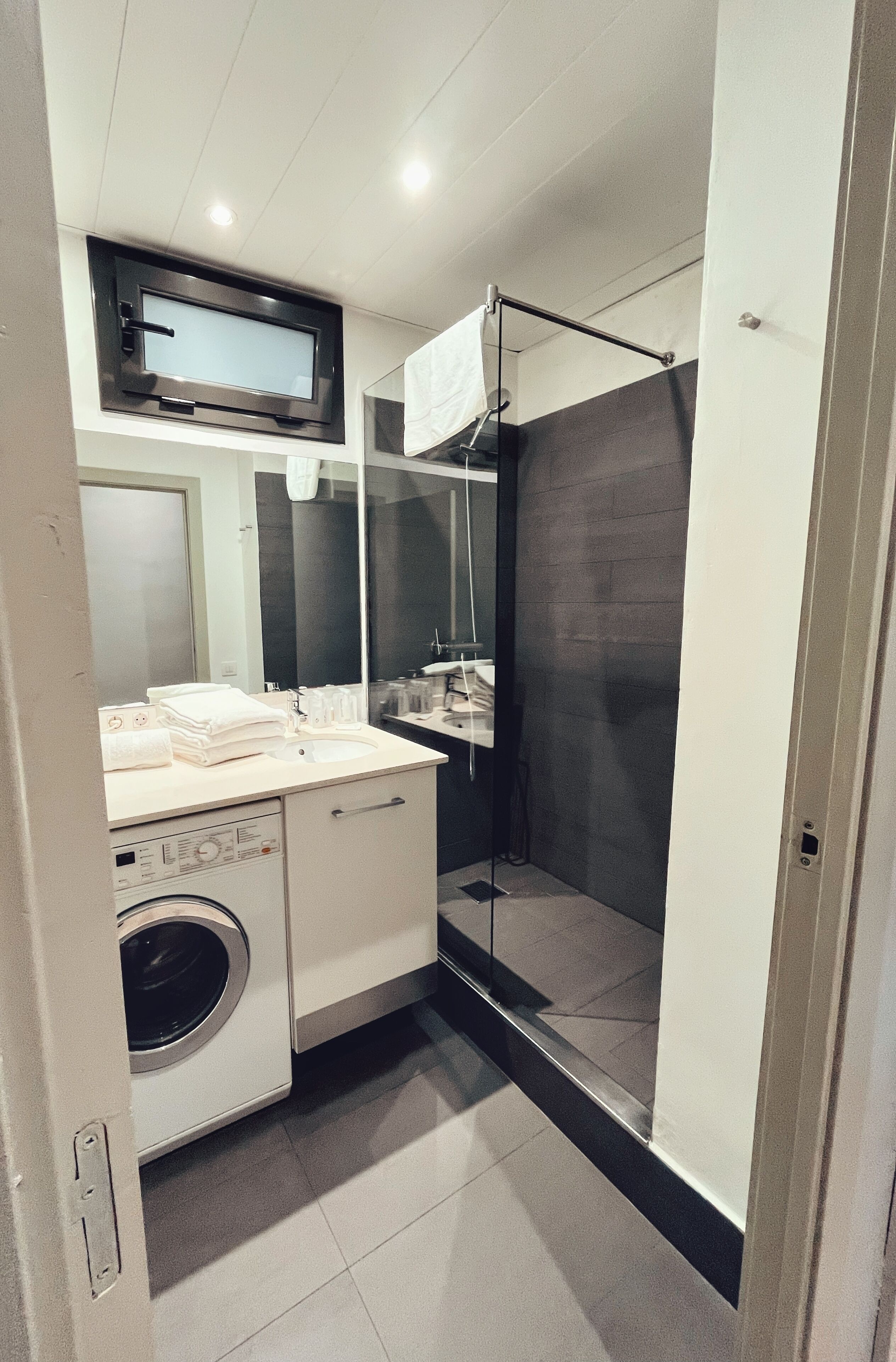 Un baño pequeño con lavadora, lavabo, espejo y cabina de ducha.