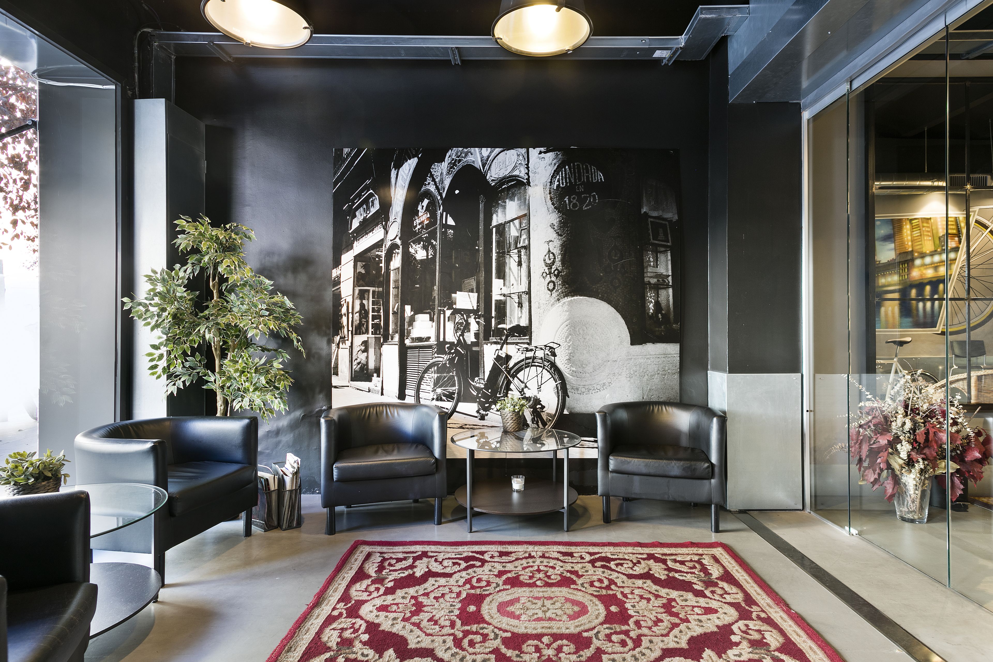 Un hall d’entrée moderne agrémenté d’une grande fresque murale, de deux canapés en cuir, d’une table basse en verre et d’un tapis rouge à motifs.