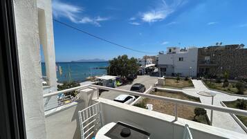 Ein Balkon mit Tisch und Stuhl, mit Blick auf eine Küstenlandschaft mit Gebäuden und geparkten Autos.