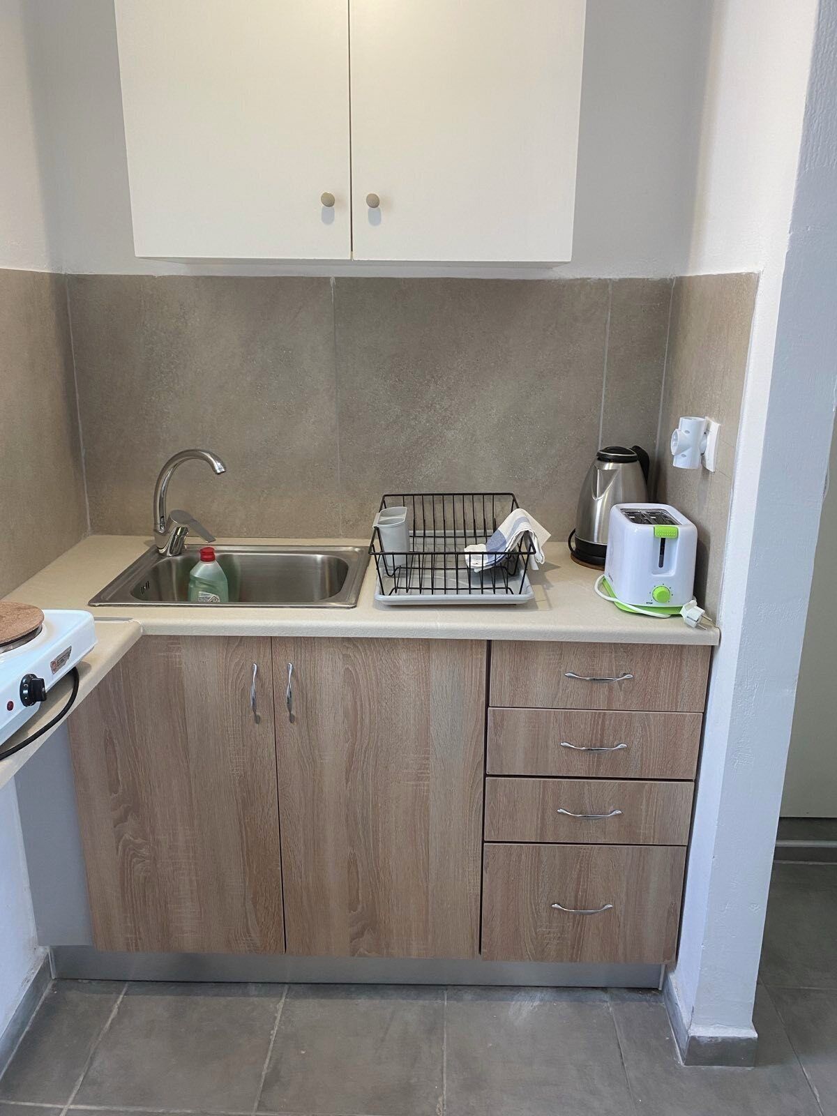 Eine kleine Küche mit Spüle, Wasserkocher, Toaster und Geschirrgestell.