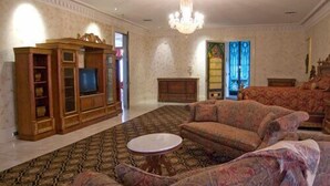 A living room with a fireplace, a television, patterned sofas, and a chandelier. - The Dansereau House (Thibodaux)